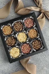 Photo of Delicious flower shaped chocolate bonbons in box and bow on grey textured background, top view