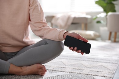 Photo of Woman with smartphone meditating on floor at home, closeup