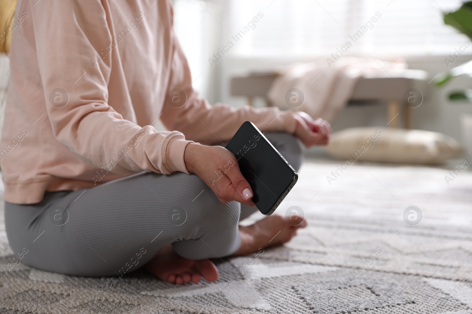 Photo of Woman with smartphone meditating on floor at home, closeup