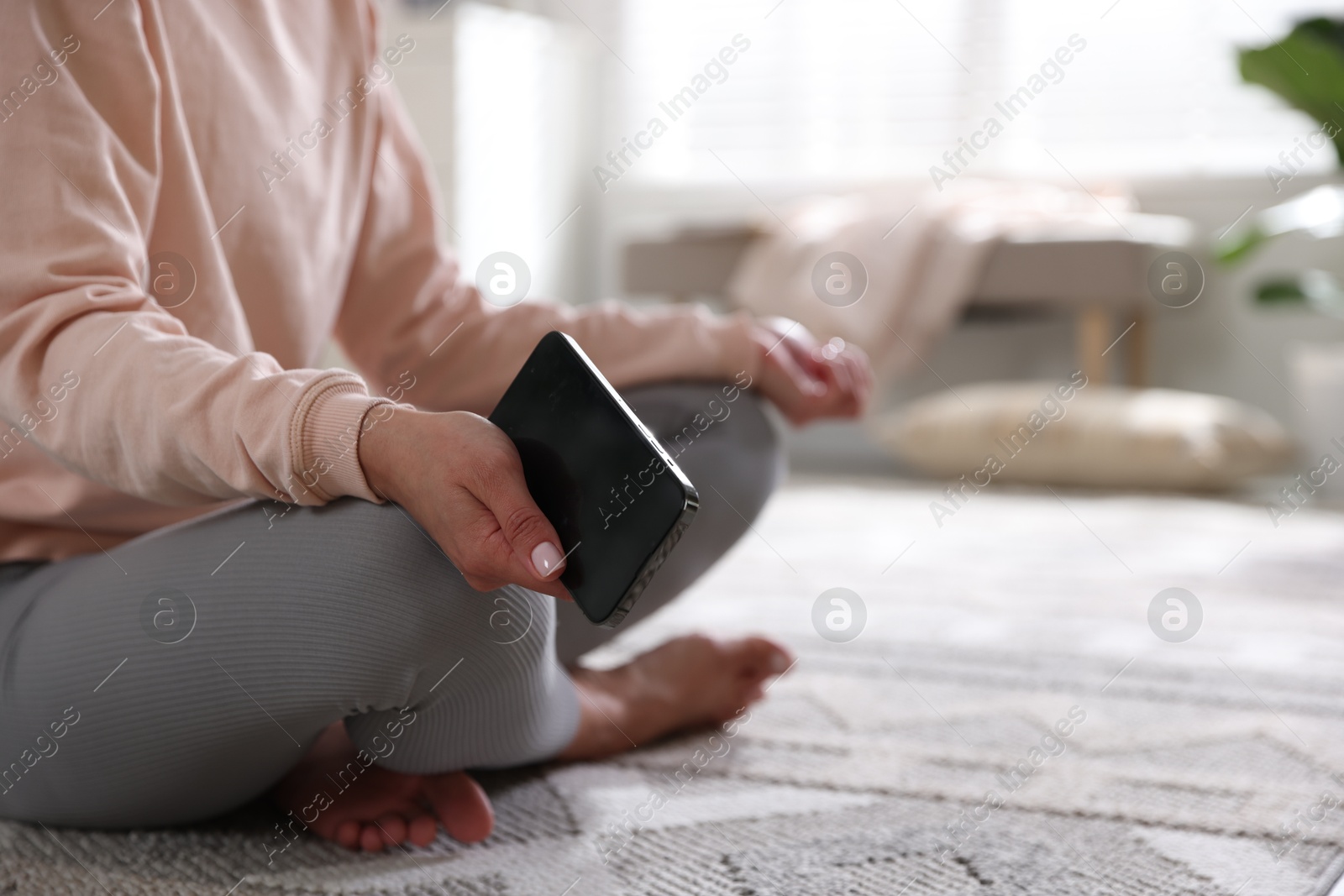 Photo of Woman with smartphone meditating on floor at home, closeup. Space for text