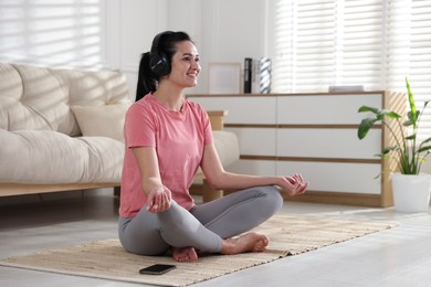 Photo of Woman with smartphone meditating on floor at home