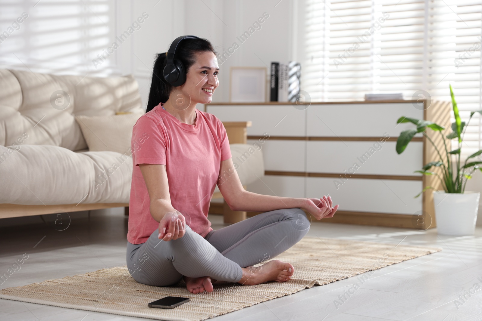 Photo of Woman with smartphone meditating on floor at home