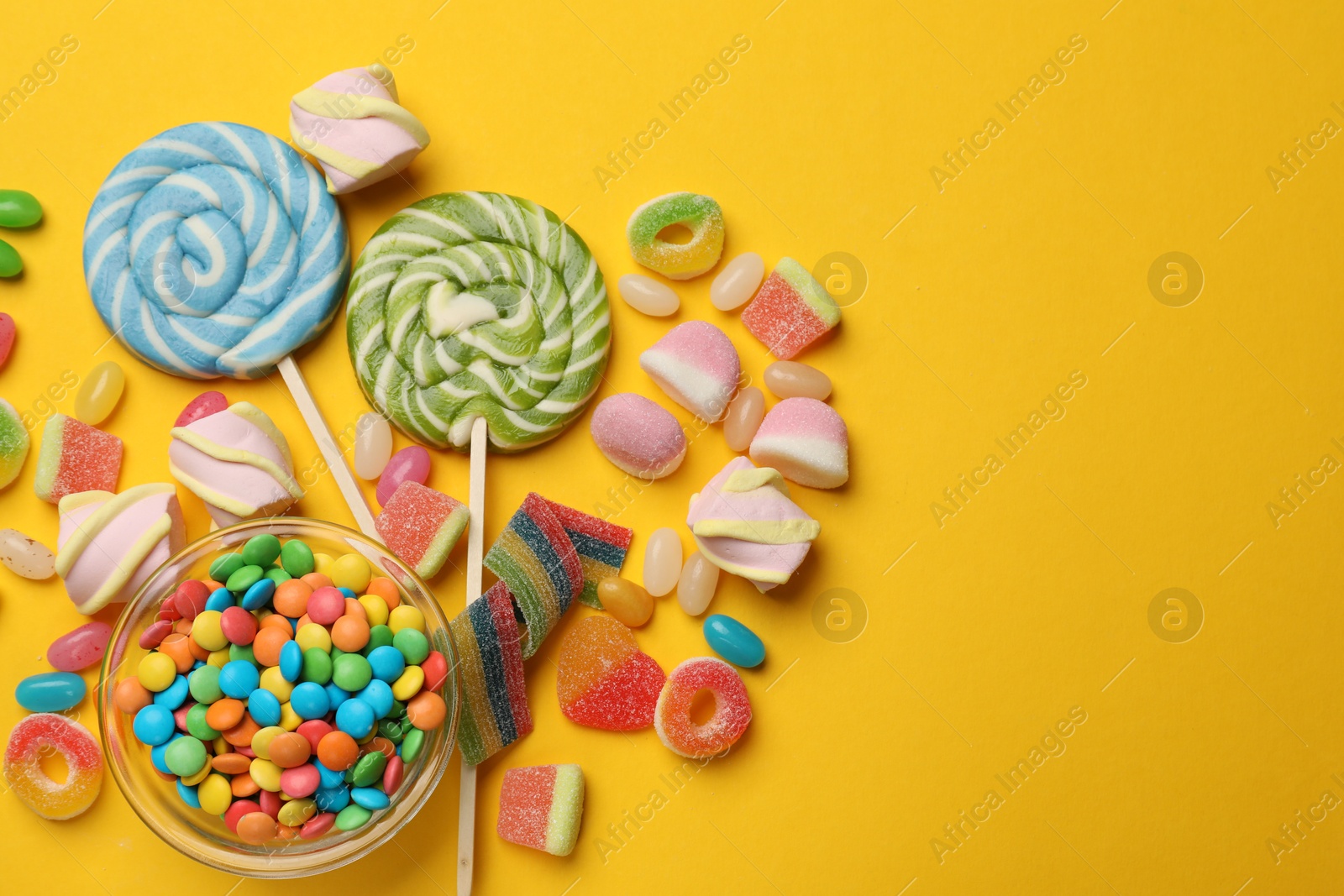 Photo of Many different tasty candies and marshmallows on yellow background, flat lay. Space for text