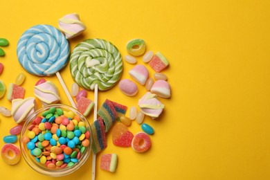 Photo of Many different tasty candies and marshmallows on yellow background, flat lay. Space for text