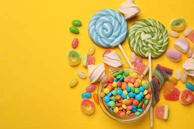 Photo of Many different tasty candies and marshmallows on yellow background, flat lay. Space for text