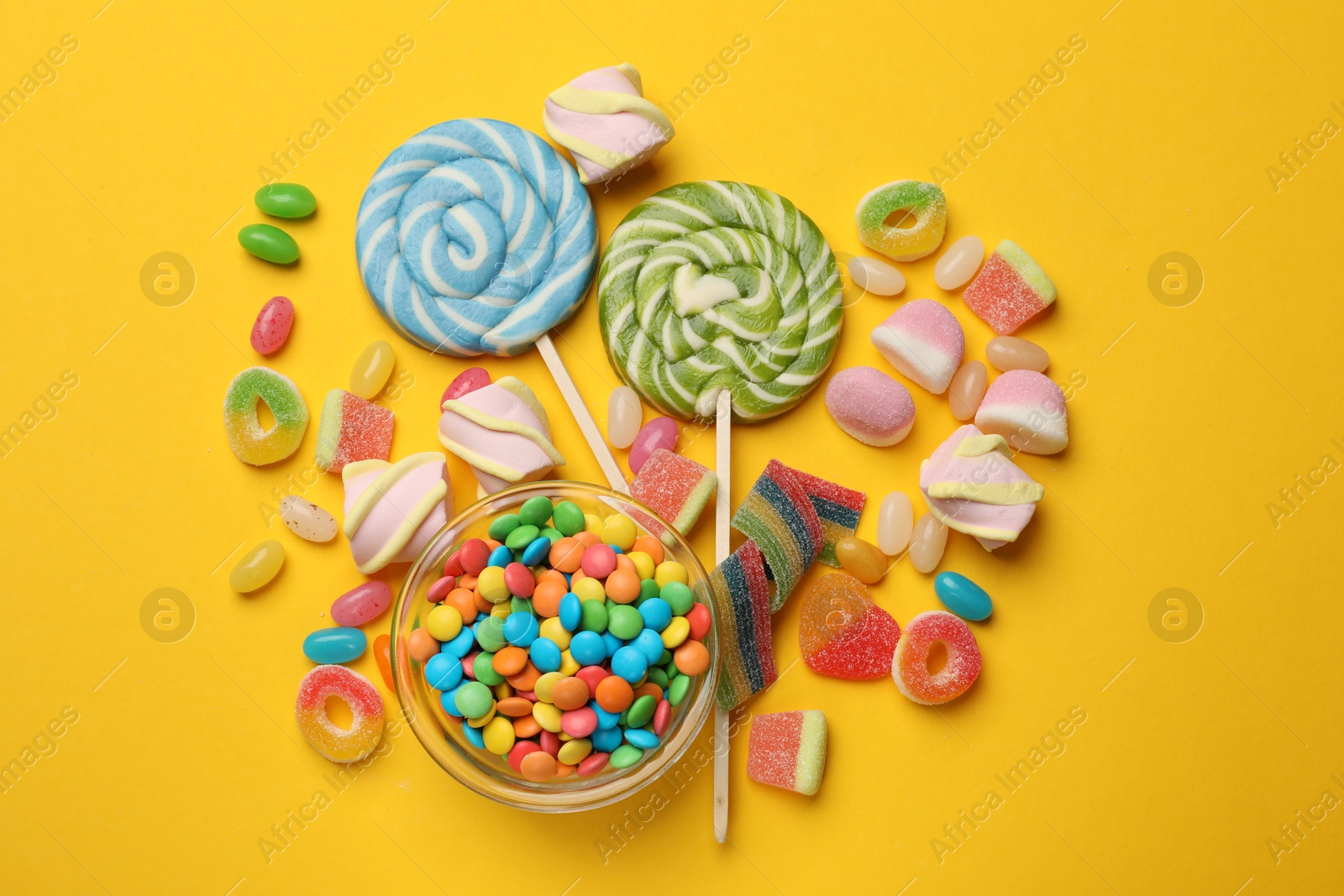 Photo of Many different tasty candies and marshmallows on yellow background, flat lay