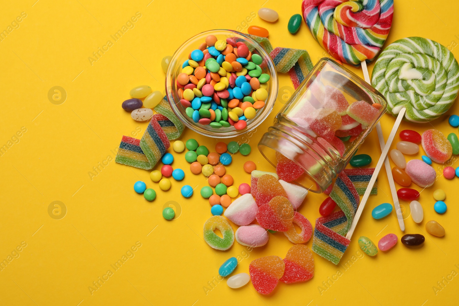 Photo of Many different tasty candies on yellow background, flat lay. Space for text