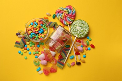 Photo of Many different tasty candies on yellow background, flat lay