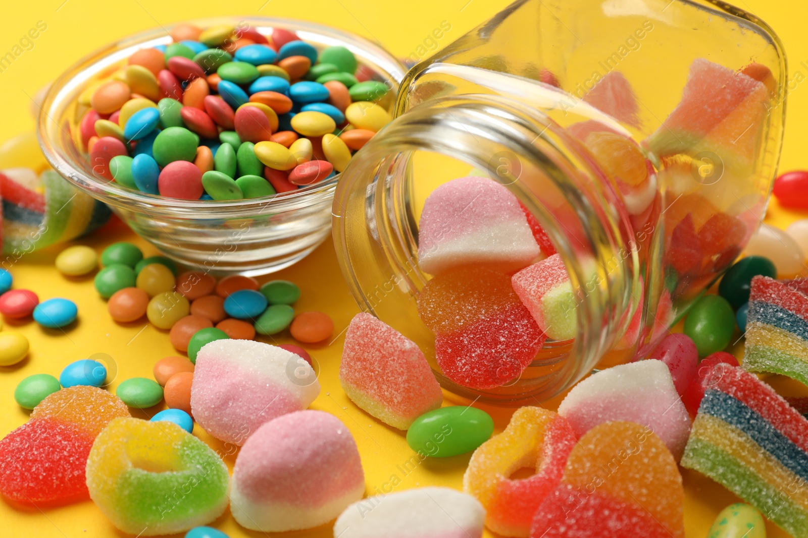 Photo of Many different tasty candies on yellow background, closeup