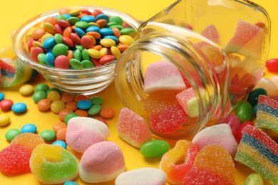 Photo of Many different tasty candies on yellow background, closeup