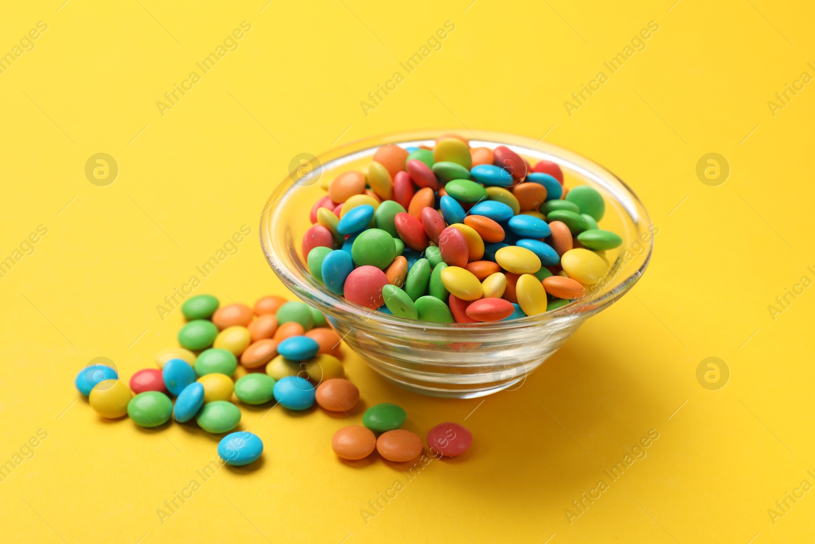 Photo of Tasty candies in bowl on yellow background, closeup