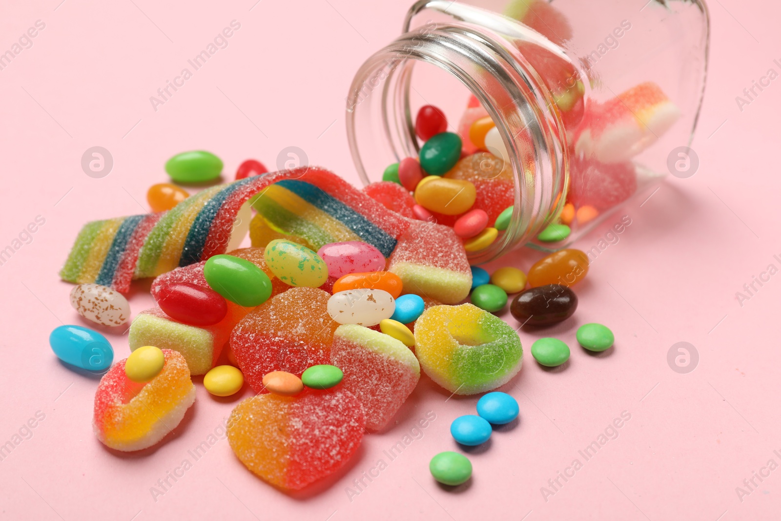 Photo of Many different tasty candies and jar on pink background, closeup