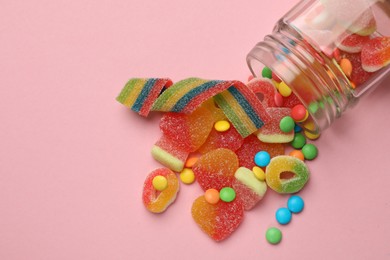 Photo of Many different tasty candies and jar on pink background, flat lay. Space for text