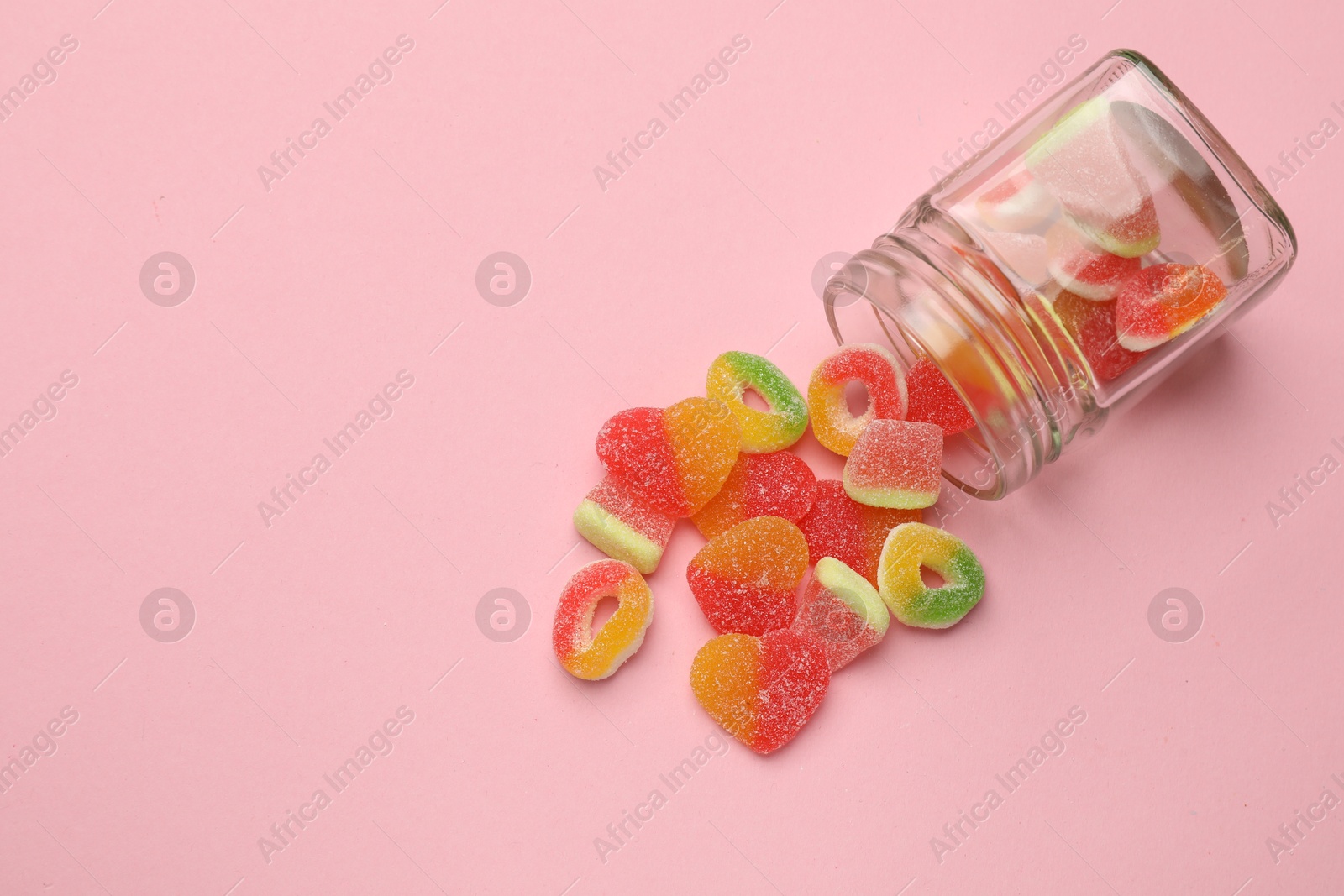 Photo of Many different tasty candies and jar on pink background, flat lay. Space for text