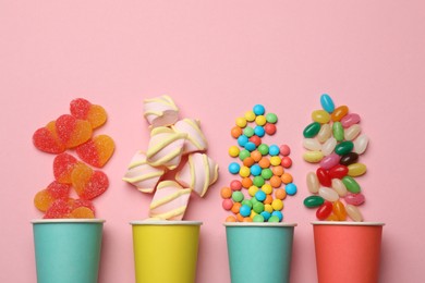 Photo of Tasty candies, marshmallows and paper cups on pink background, flat lay. Space for text