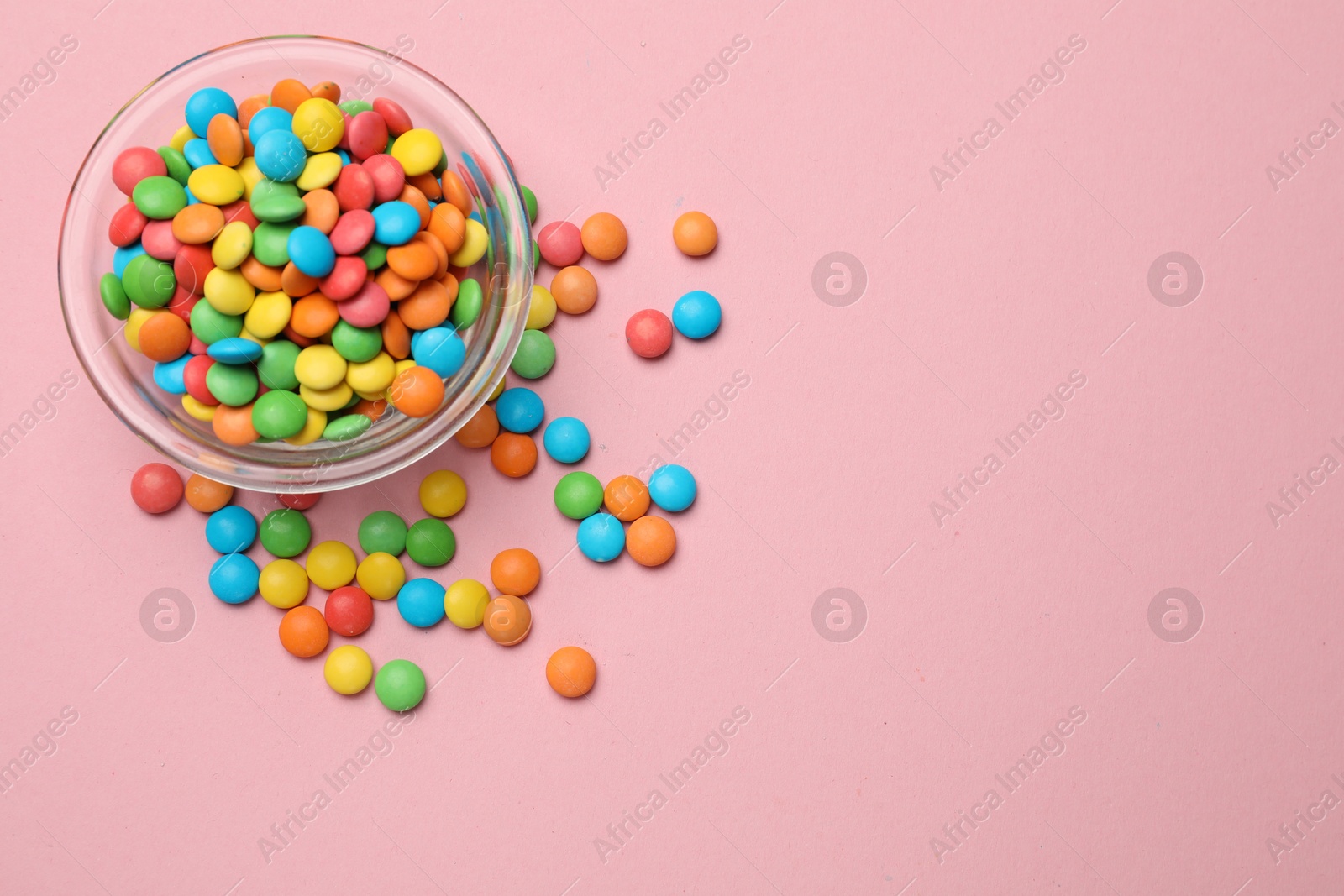 Photo of Tasty candies in bowl on pink background, top view. Space for text