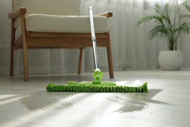 Photo of Microfiber mop on floor near armchair indoors. Cleaning equipment