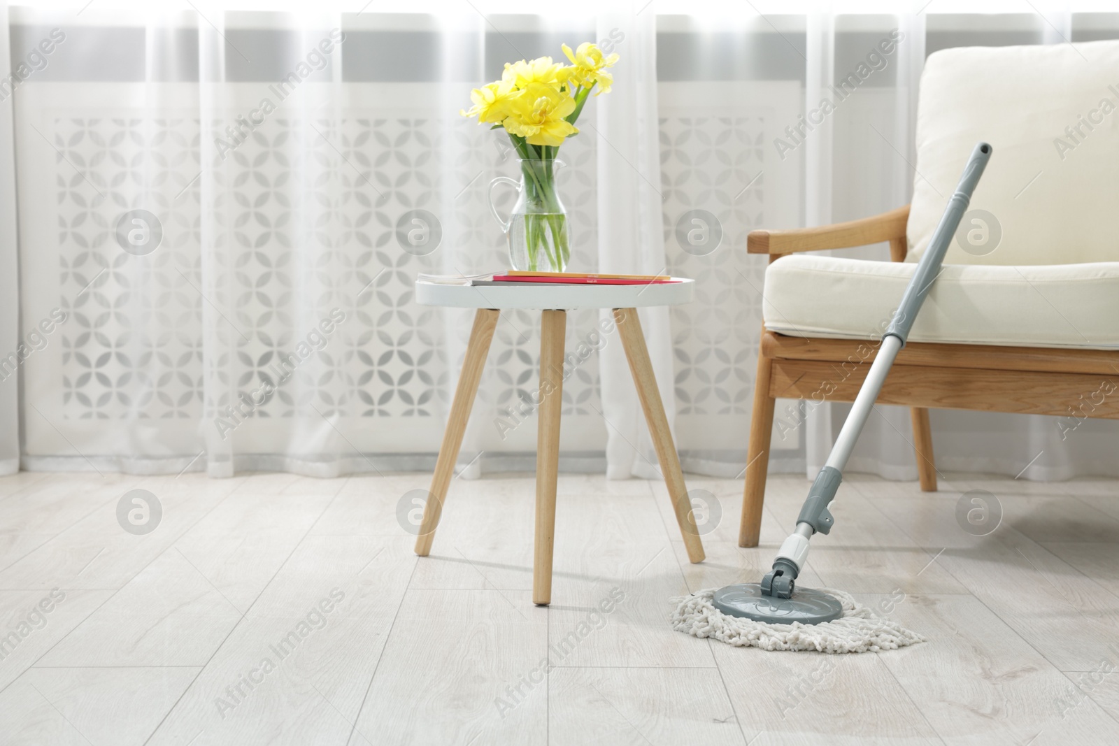 Photo of String mop on floor near armchair and side table with flowers indoors, space for text