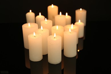 Photo of Many burning candles on mirror surface in darkness