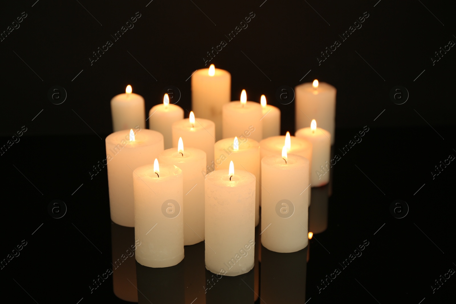 Photo of Many burning candles on mirror surface in darkness