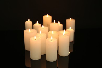 Photo of Many burning candles on mirror surface in darkness