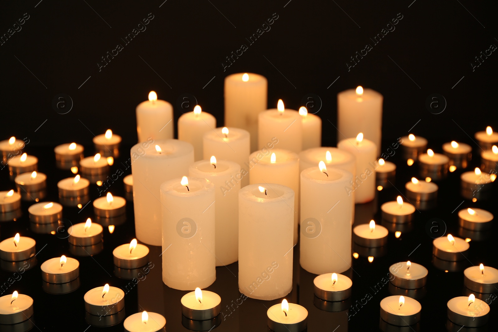 Photo of Many burning candles on mirror surface in darkness