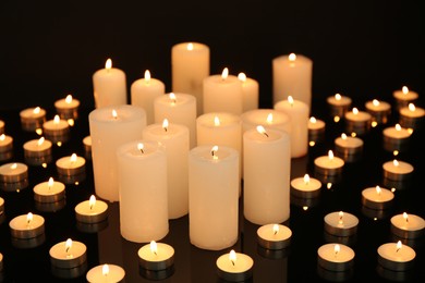 Photo of Many burning candles on mirror surface in darkness