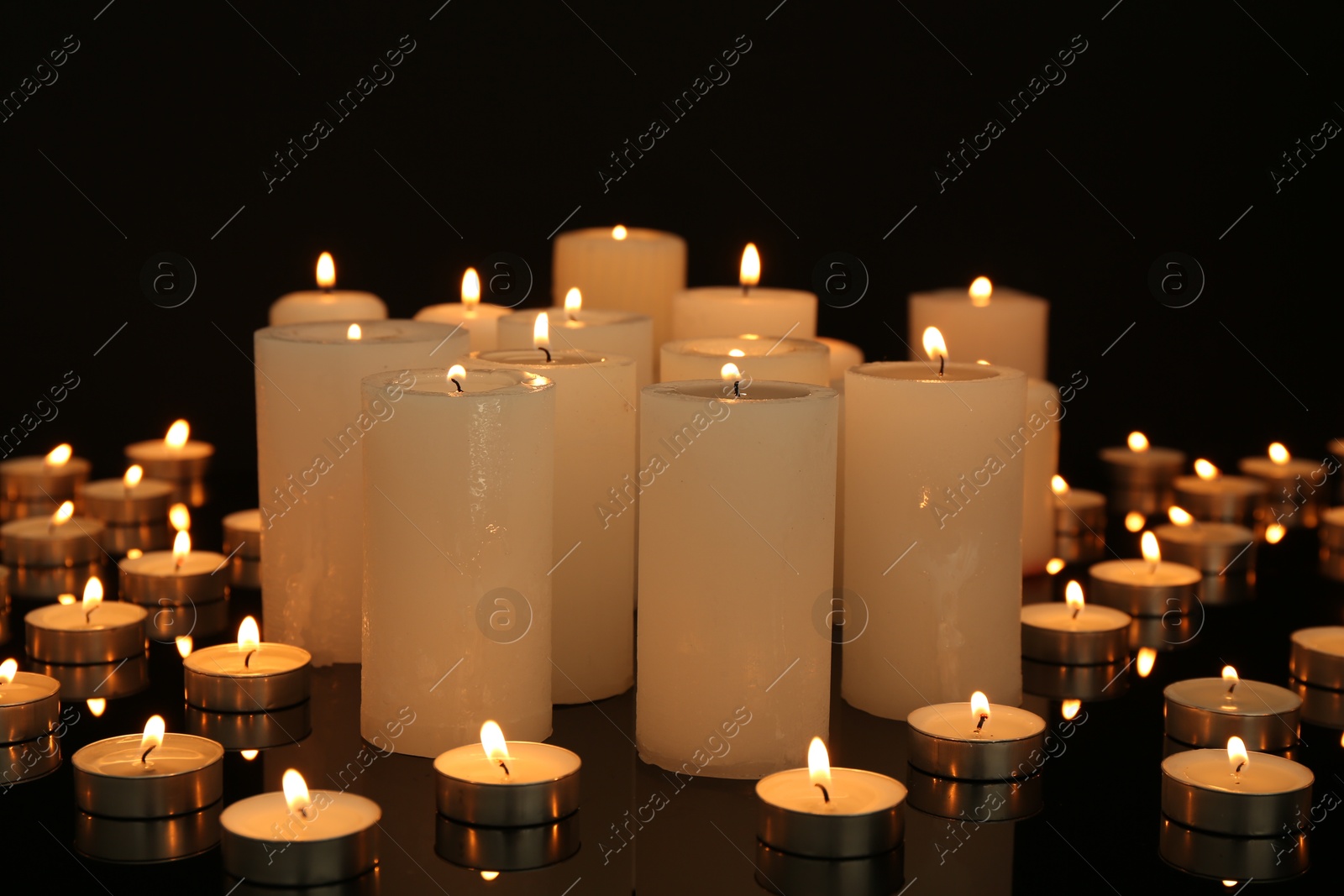 Photo of Many burning candles on mirror surface in darkness