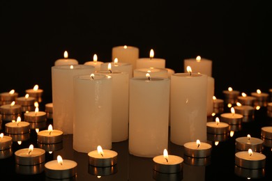 Photo of Many burning candles on mirror surface in darkness