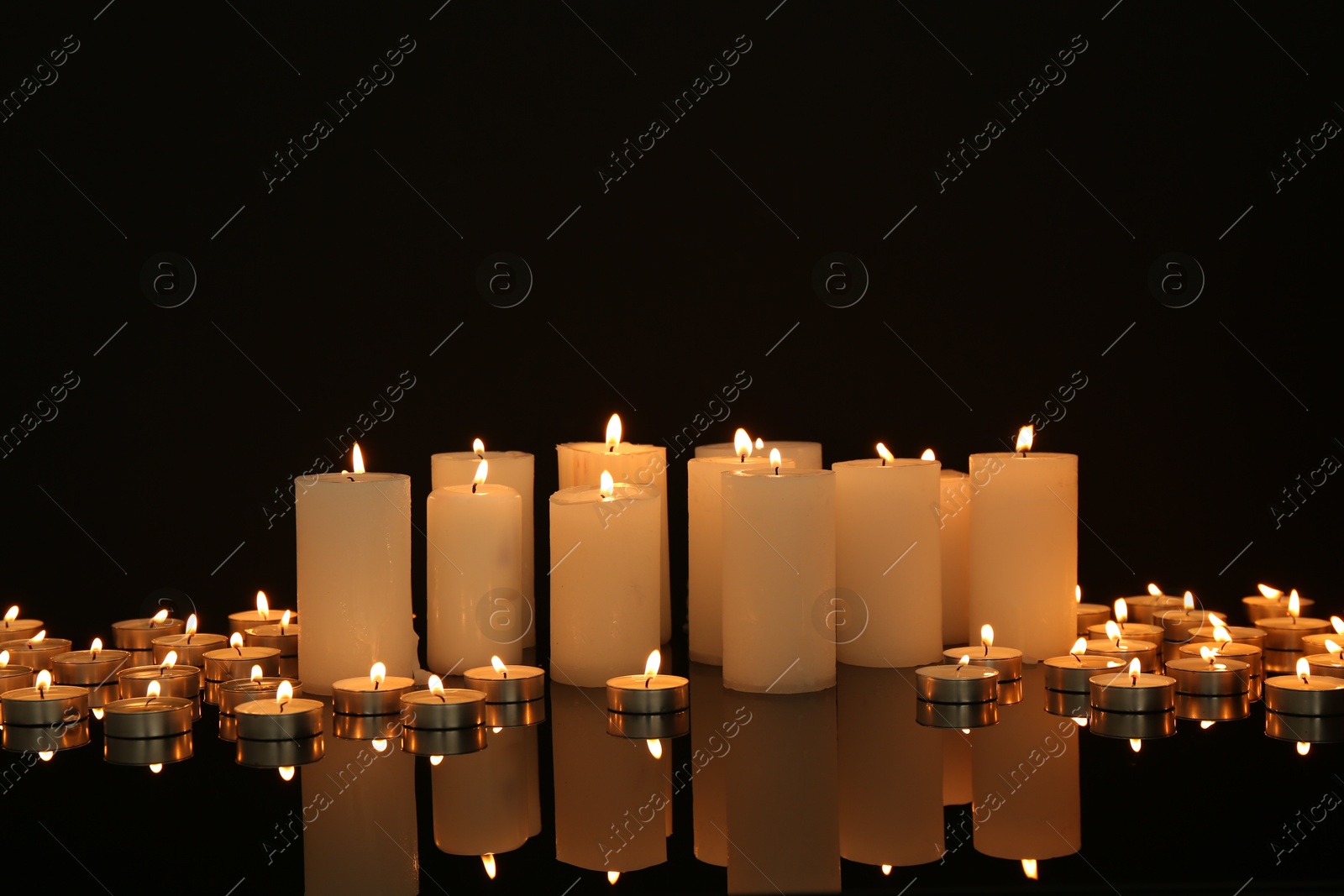 Photo of Many burning candles on mirror surface in darkness