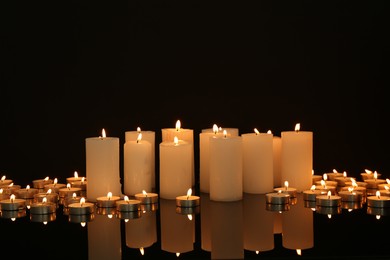 Photo of Many burning candles on mirror surface in darkness