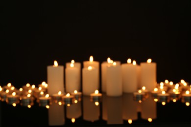 Photo of Blurred view of burning candles on mirror surface in darkness