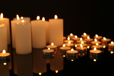 Photo of Blurred view of burning candles on mirror surface in darkness