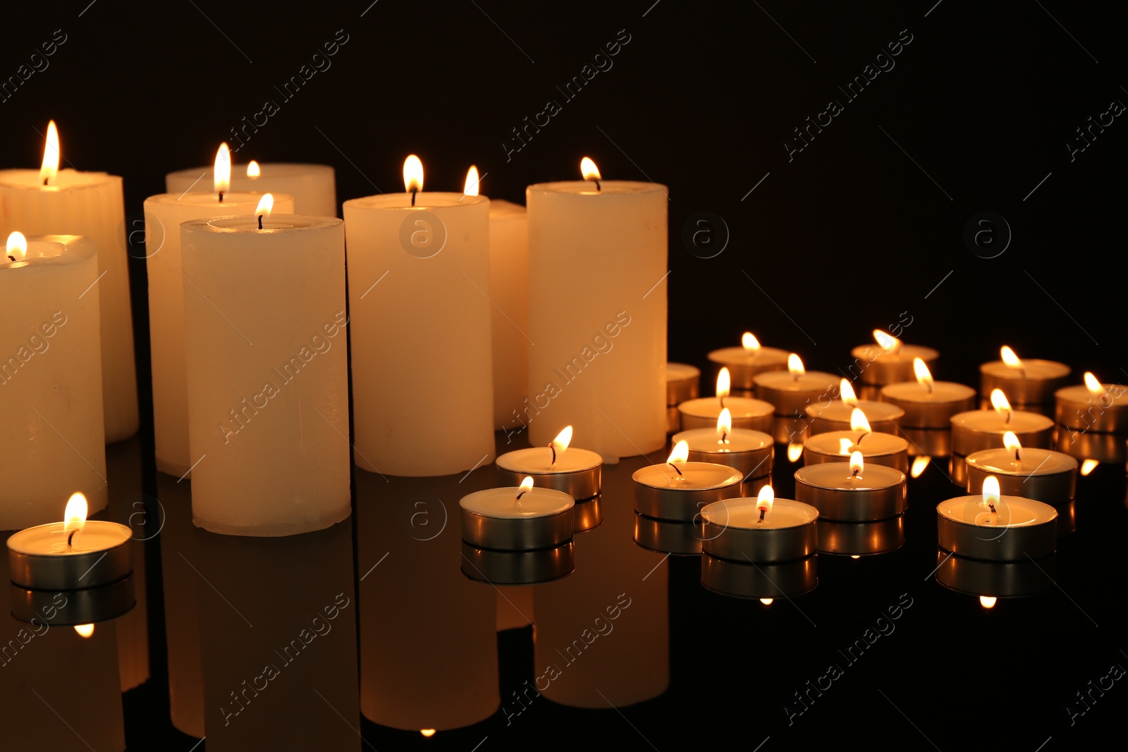 Photo of Many burning candles on mirror surface in darkness