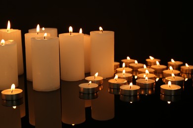 Photo of Many burning candles on mirror surface in darkness