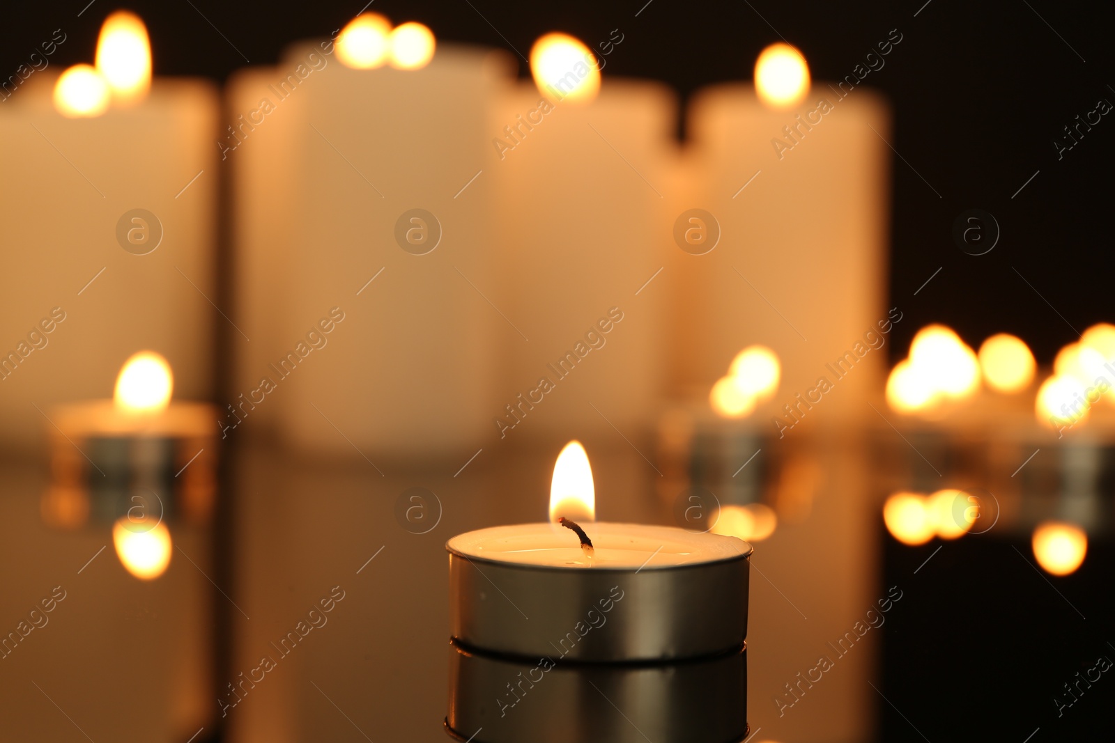 Photo of Burning candles on dark mirror surface, closeup