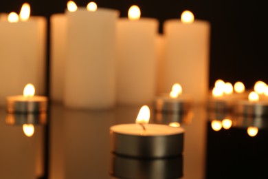 Photo of Blurred view of burning candles on dark mirror surface