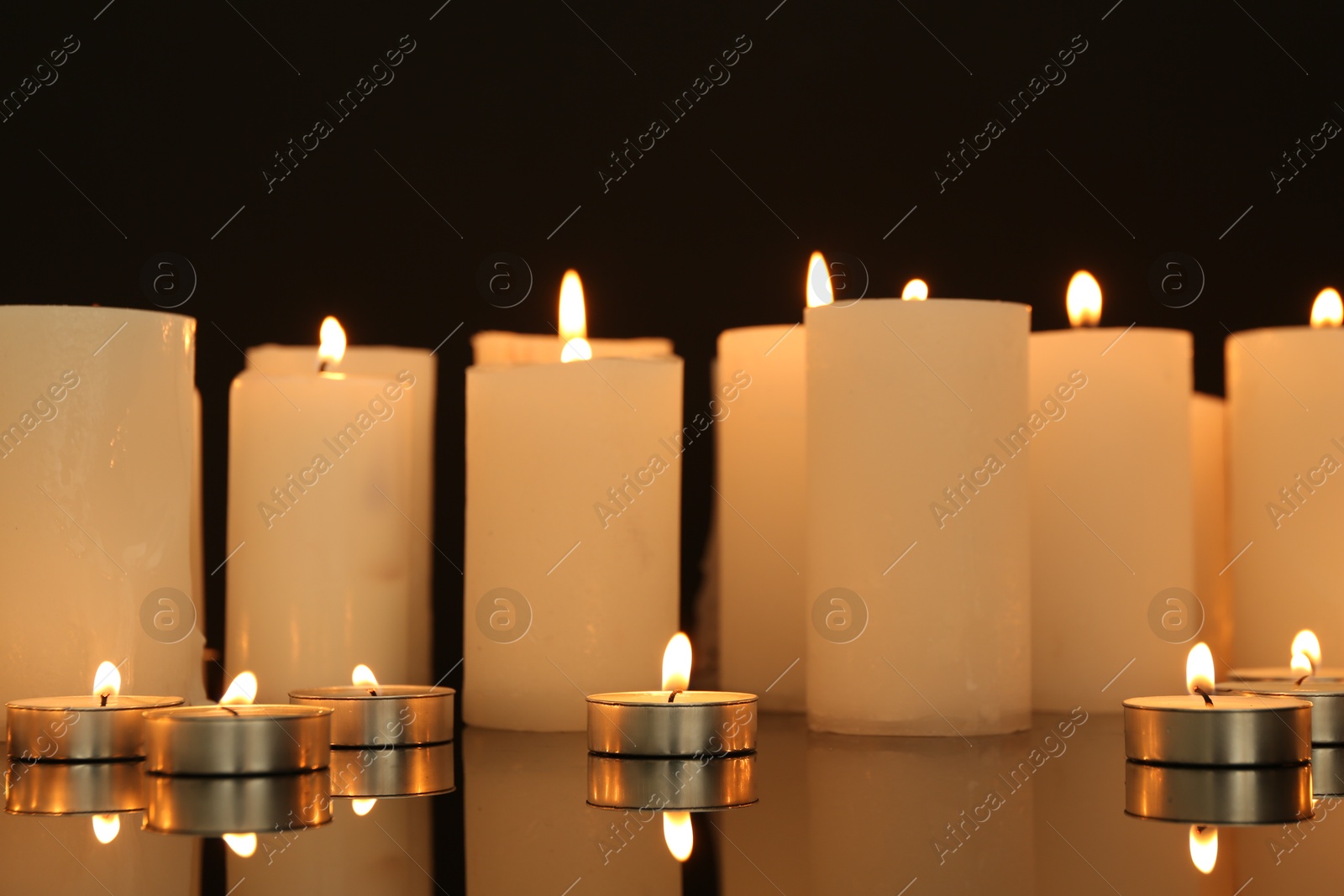 Photo of Many burning candles on mirror surface against black background