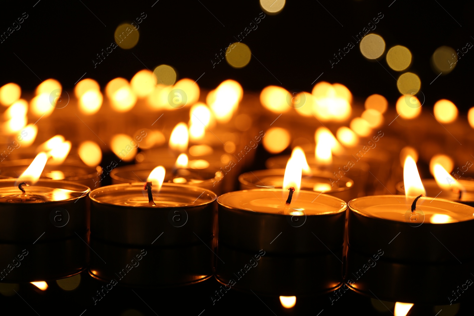 Photo of Many burning candles in darkness, closeup view