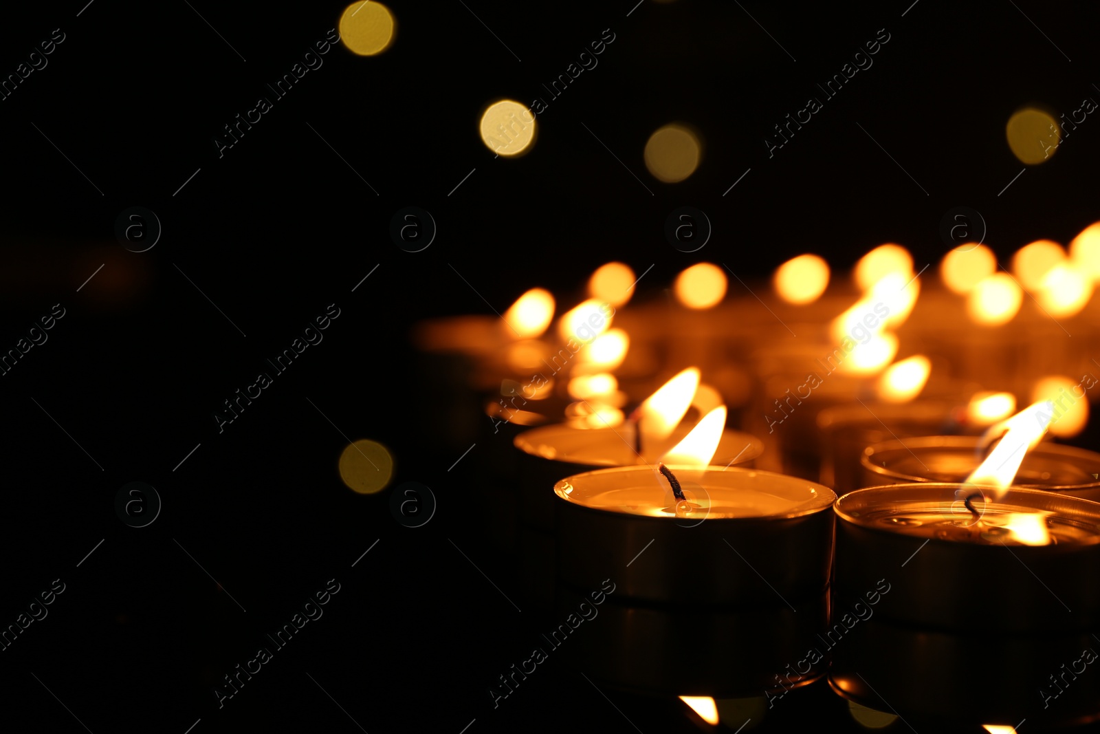 Photo of Many burning candles in darkness, closeup. Space for text