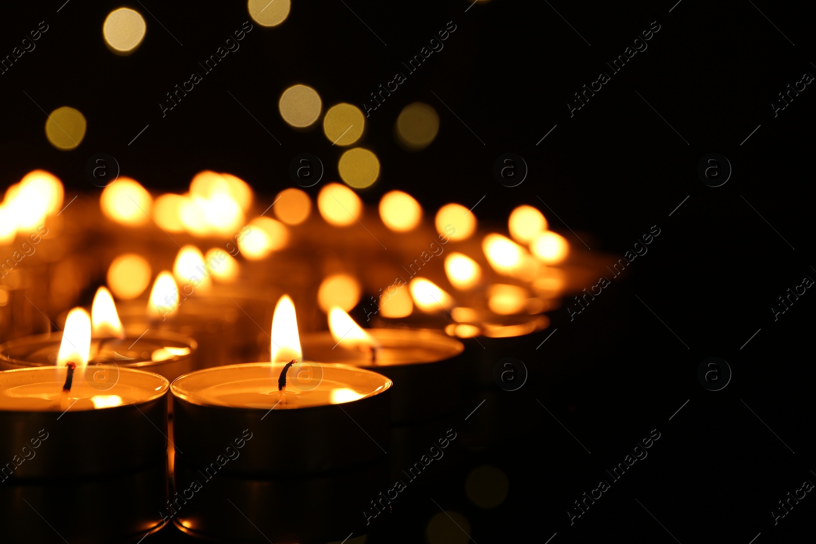 Photo of Many burning candles in darkness, closeup. Space for text