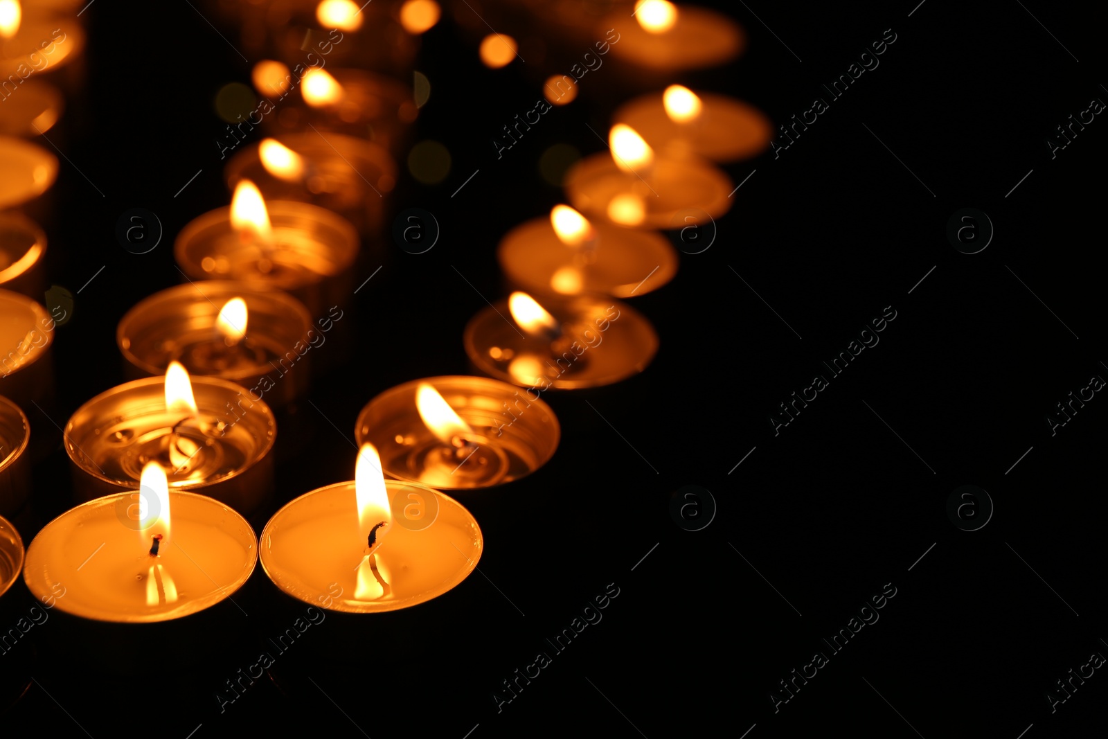 Photo of Many burning candles in darkness, closeup. Space for text