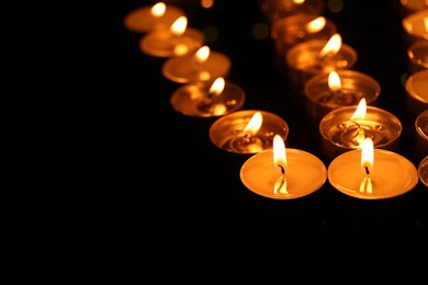 Photo of Many burning candles in darkness, closeup. Space for text