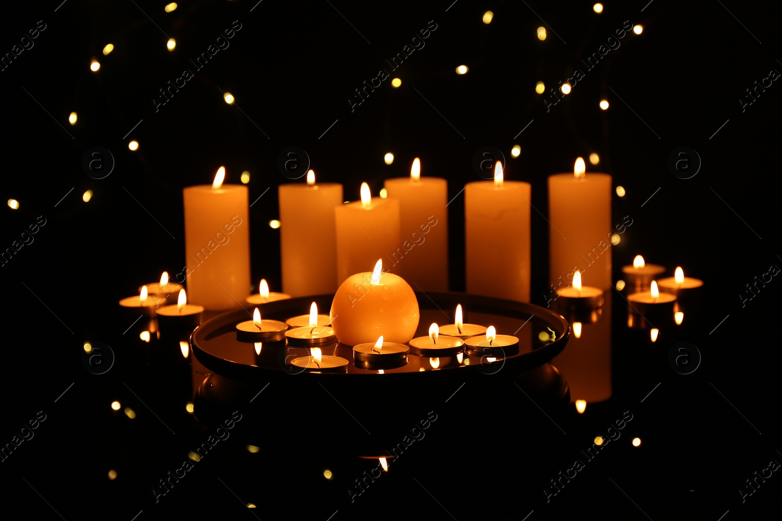 Photo of Many burning candles on mirror surface in darkness