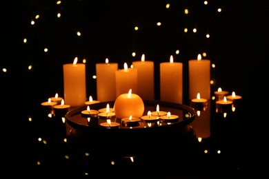 Photo of Many burning candles on mirror surface in darkness