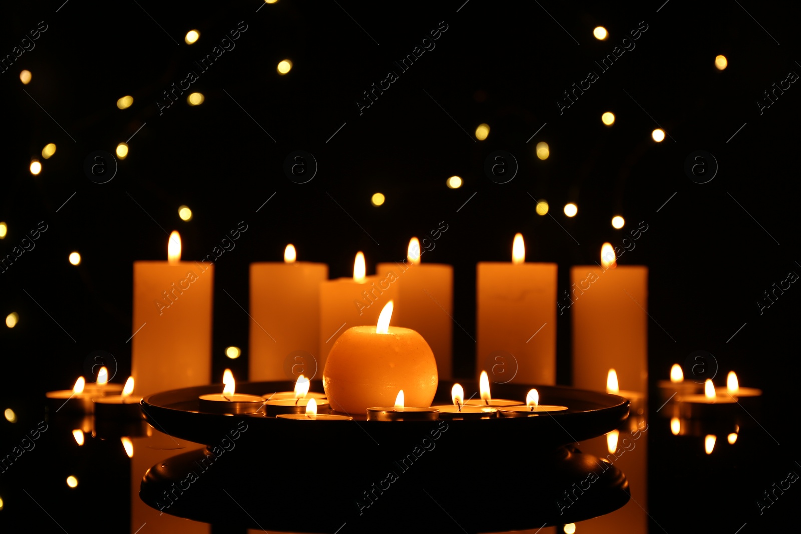 Photo of Many burning candles on mirror surface in darkness