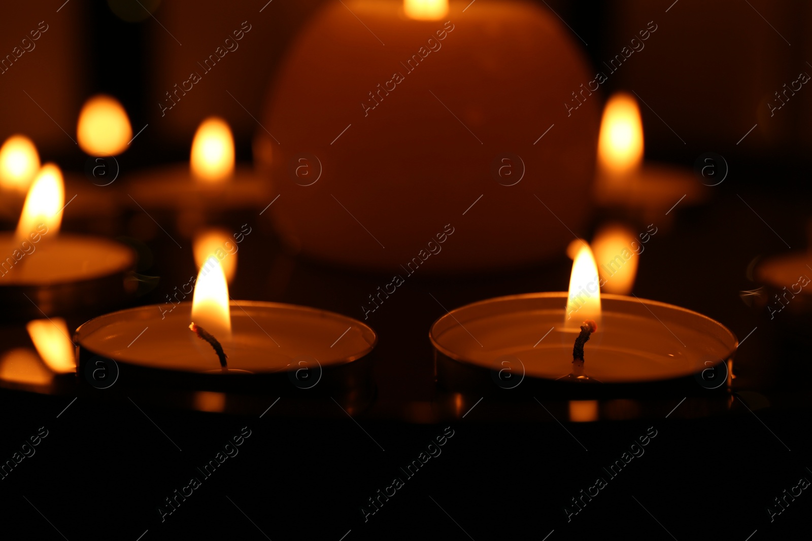 Photo of Many burning candles on dark surface, closeup