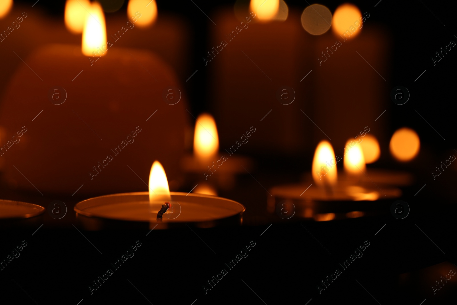 Photo of Many burning candles on dark surface, closeup