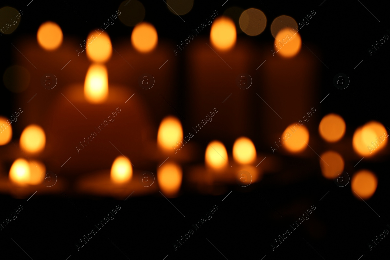 Photo of Blurred view of burning candles in darkness, bokeh effect