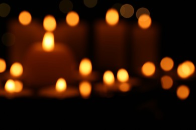 Photo of Blurred view of burning candles in darkness, bokeh effect